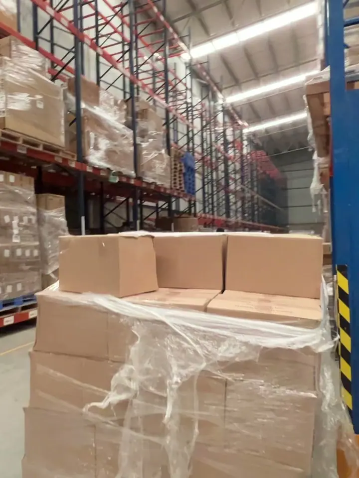 Tarima de cajas de cartón envuelta en película plástica junto a un rack