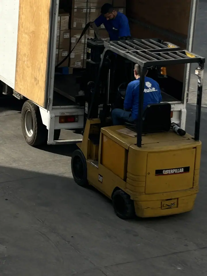 Operador de Mubit en un montacargas amarillo descargando un camión de caja, con otro operador dentro del camión