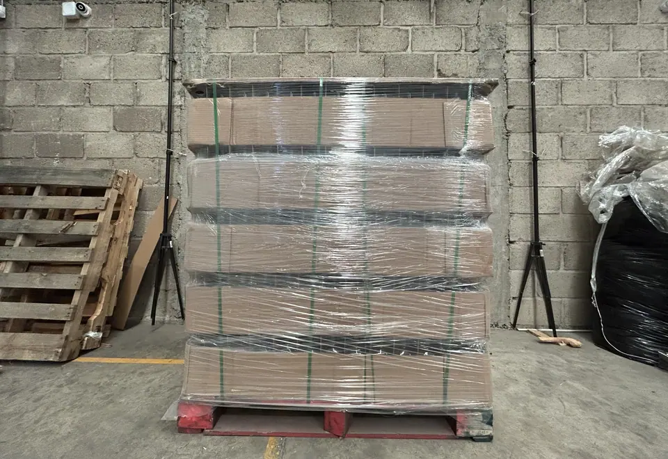 Una tarima de cajas de cartón emplayada y flejada sobre su tarima roja, frente a un muro de block